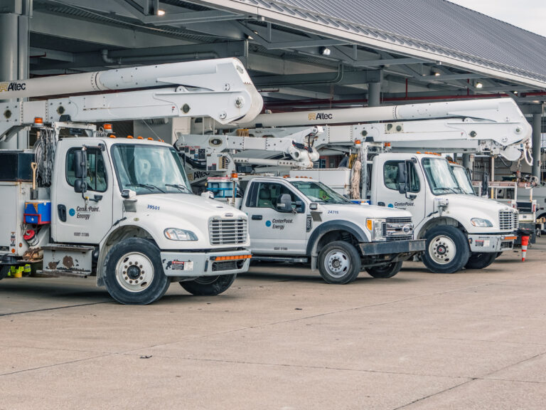 White utility trucks with company logos on their doors, parked outside a service building.