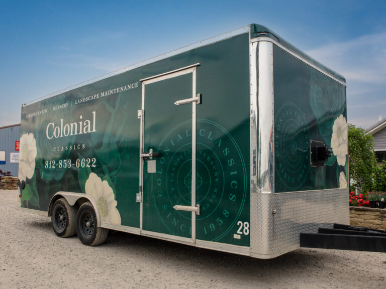 Enclosed trailer wrapped in green Colonial Classics graphics with white flowers.