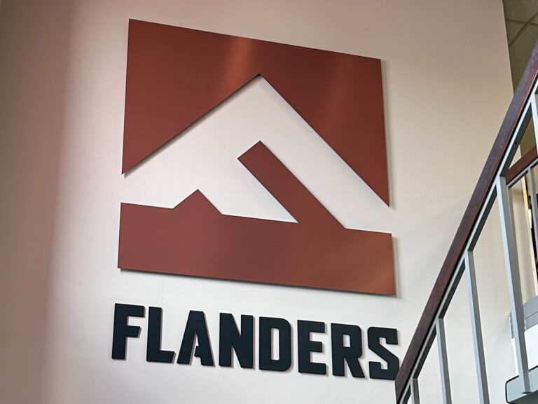 Dimensional Flanders logo and lettering mounted on an interior wall beside a staircase.