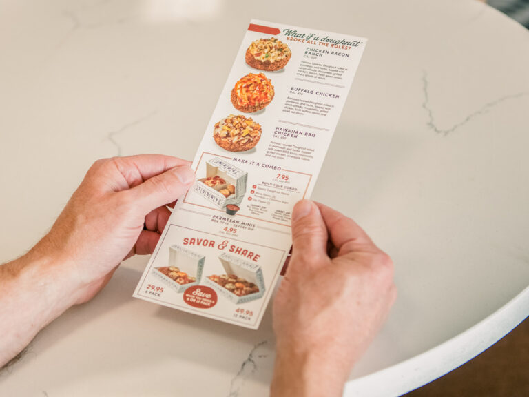 Hands holding a printed menu with food photos and descriptions.
