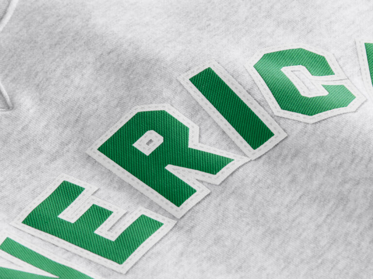 Green fabric letters with white stitched borders appliqued onto gray apparel.