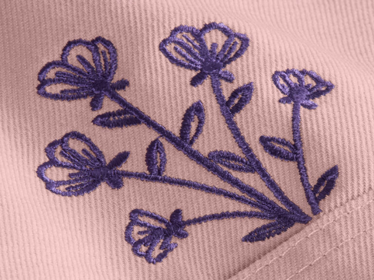 Purple flowers embroidered in flat stitches on pink fabric.