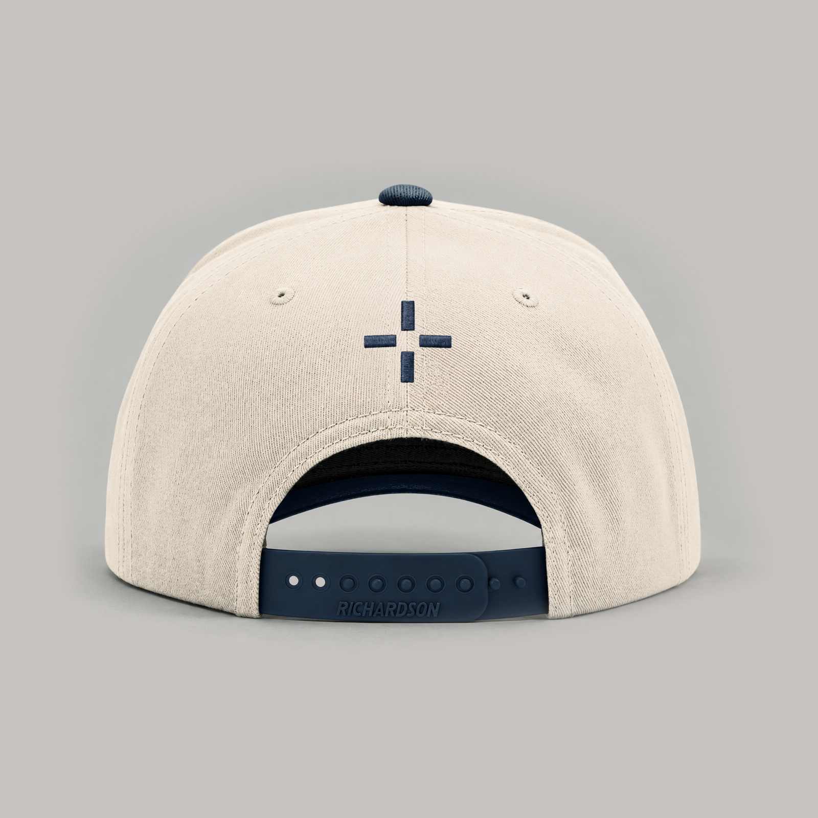 Cream cap with a small embroidered geometric logo above the navy back strap.