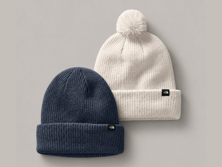 Navy cuffed knit beanie beside a cream pom-pom beanie.