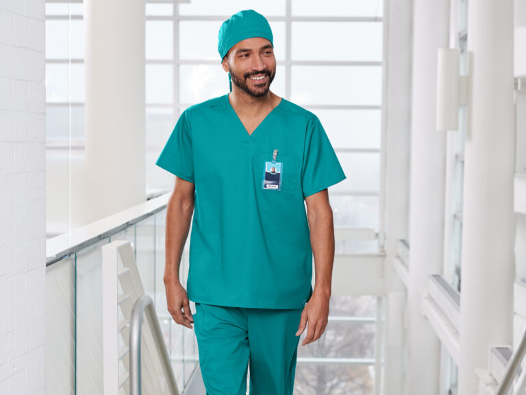 Person wearing teal scrubs, a matching surgical cap and an ID badge in a hospital corridor.