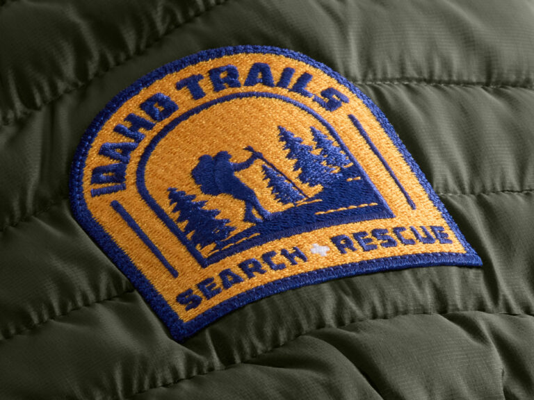Gold and blue embroidered search-and-rescue patch sewn onto an olive quilted jacket.