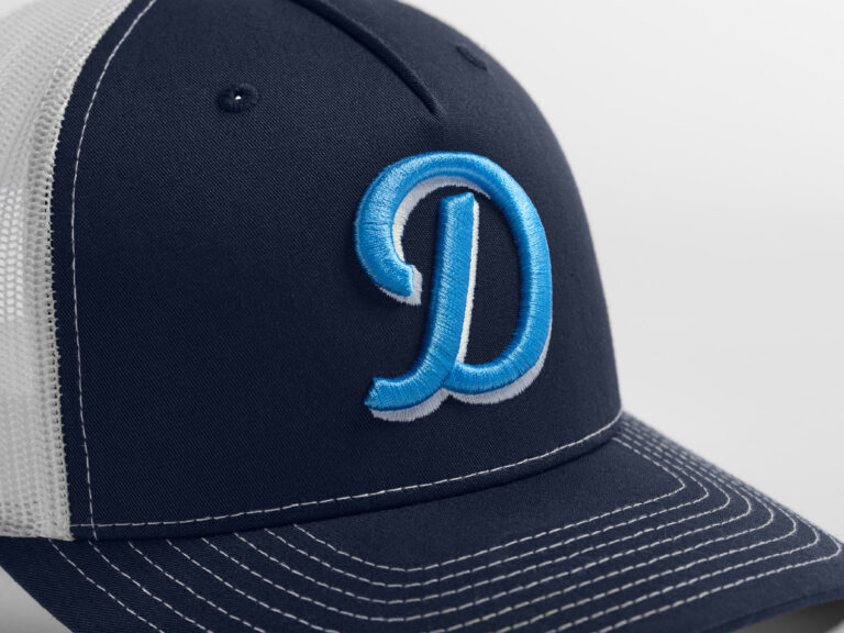 Raised blue letter D embroidered on the front of a navy trucker cap.