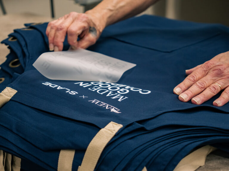 Hands peeling transfer film from a navy apron to reveal a white printed design.