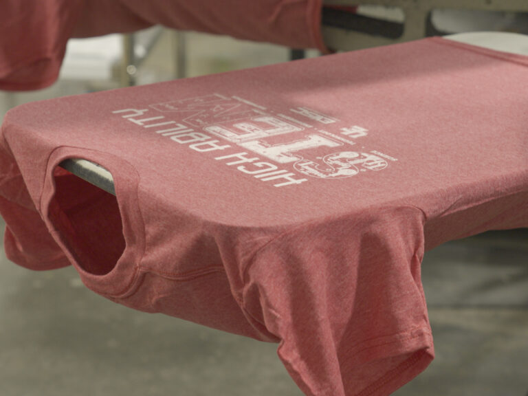 Muted red T-shirt stretched over a printing platen with a white graphic on the front.