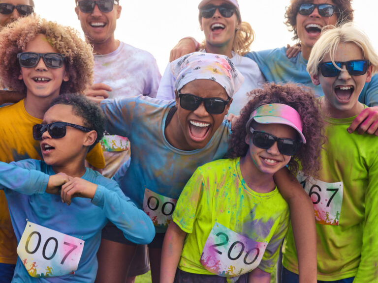 Group wearing colorful event T-shirts, sunglasses and race bibs at an outdoor run.