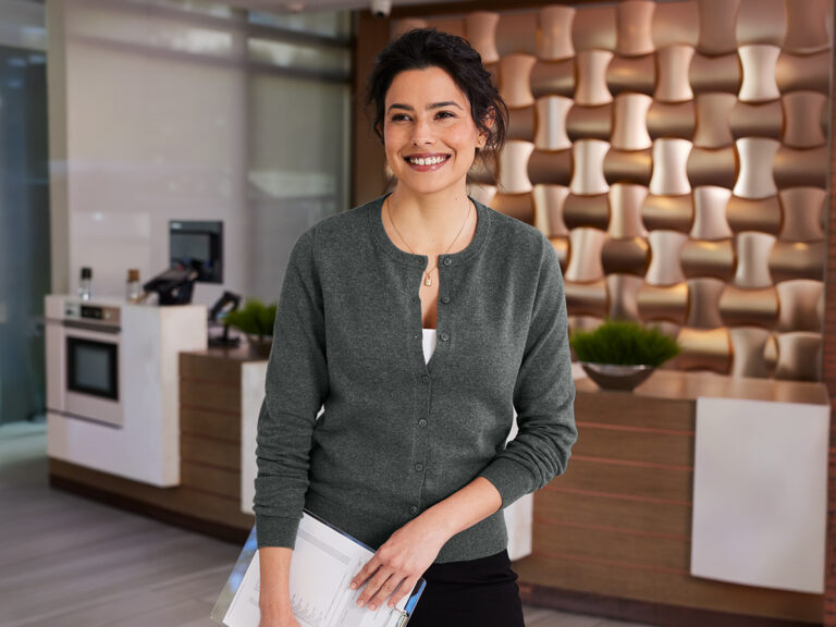 Person wearing a dark gray cardigan over a white top in an office lounge.