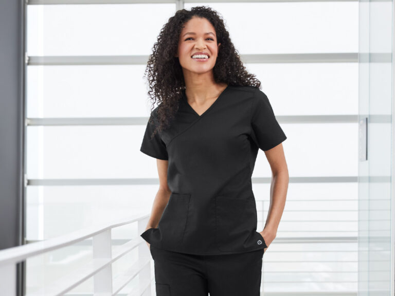 Person wearing black V-neck scrubs in a hospital corridor.