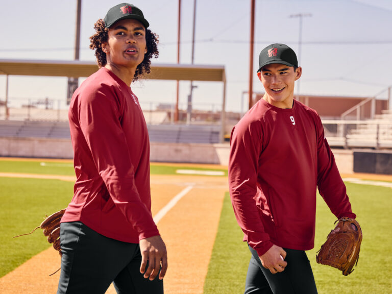 Two baseball players wearing matching red long-sleeve tops and caps, holding gloves on a field.
